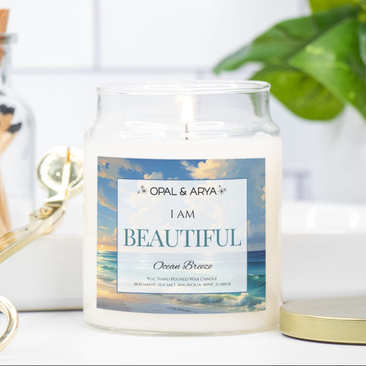 Candle with a 'I AM BEAUTIFUL' label on a white surface with a plant and matches in the background.